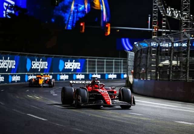 A red Ferrari Formula 1 car leading through a corner at the Las Vegas night street race, Salesforce boards and safety fencing