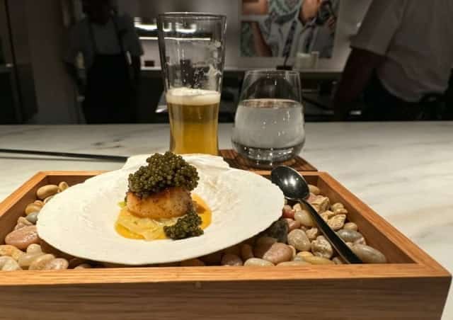 A gourmet scallop dish topped with caviar served on a shell over pebbles at a dining counter