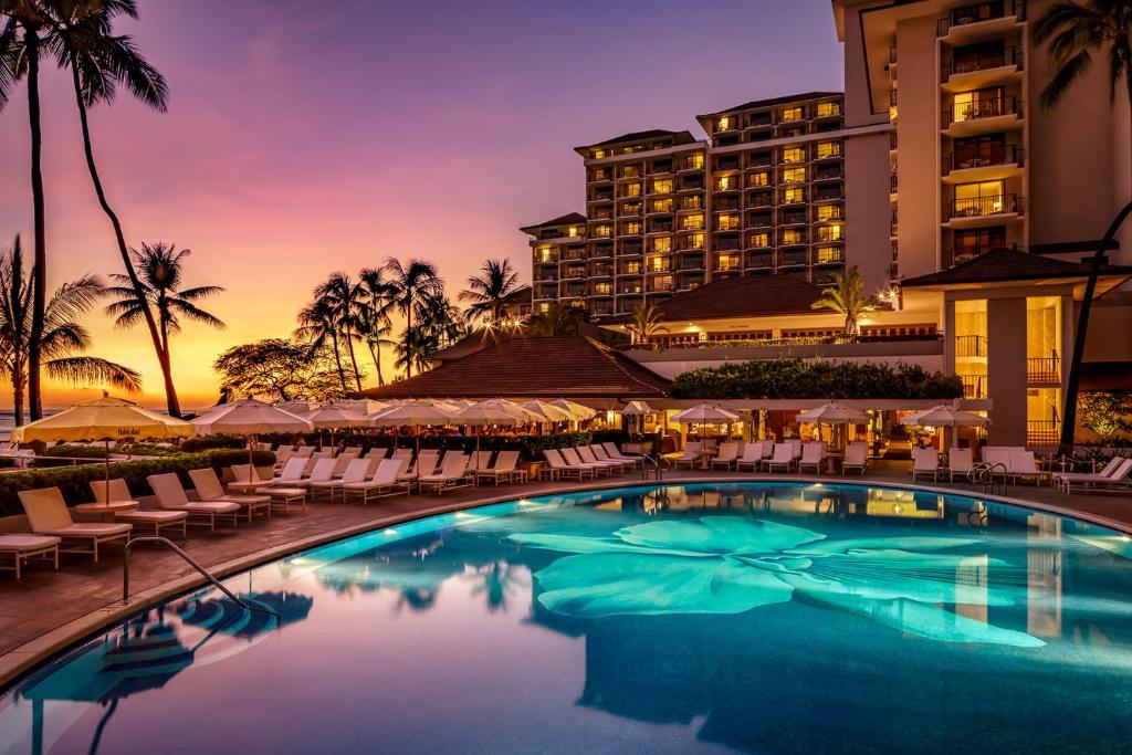 Halekulani beachfront resort at sunset with a glowing flower-mosaic pool, palm trees and a violet-gold terracotta