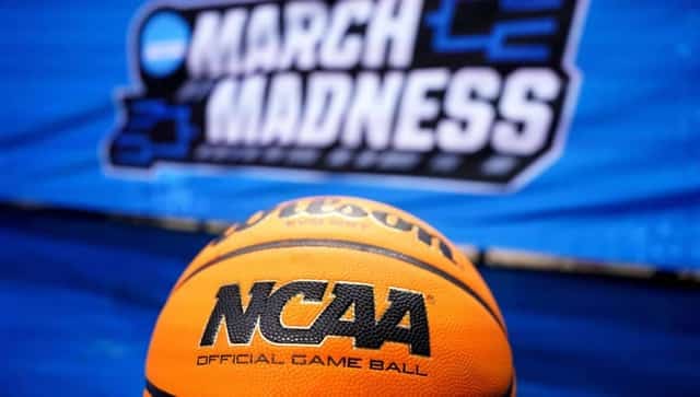 An official NCAA basketball in front of a blurred March Madness logo on blue