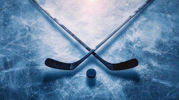 Two crossed ice hockey sticks and a black puck resting on frosty blue ice