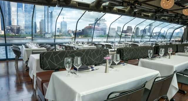 Elegant dining room aboard a New York dinner cruise with the Manhattan skyline through panoramic windows