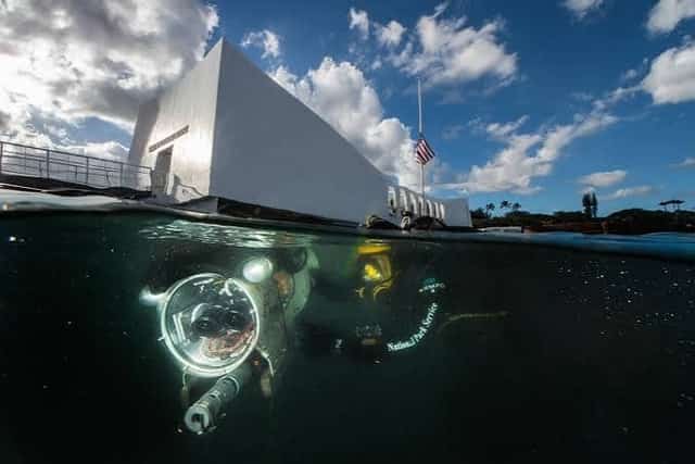 The white USS Arizona Memorial at Pearl Harbor with divers and a submersible in the water below