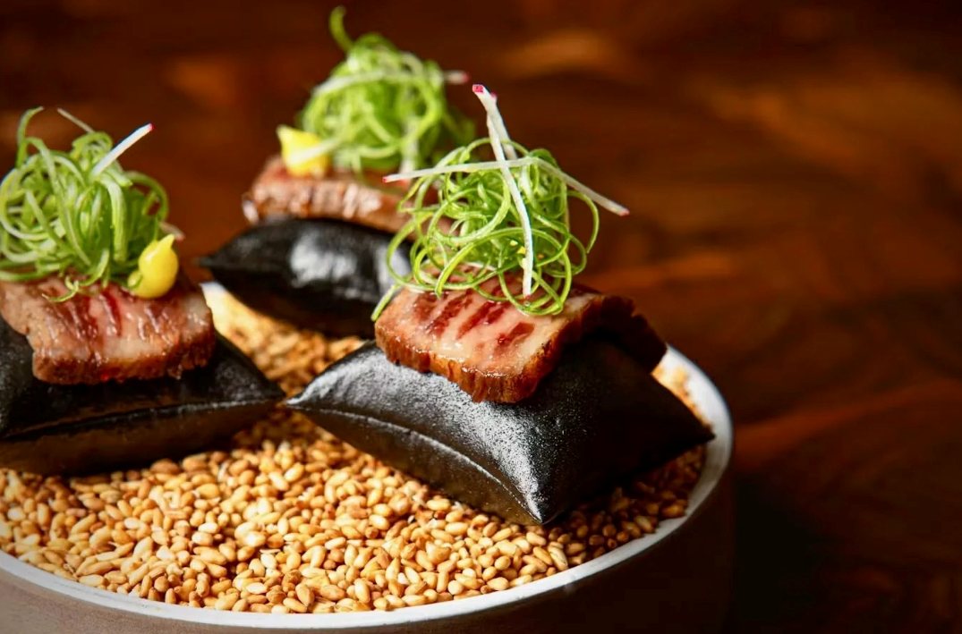 Sliced seared wagyu on black stone pillows garnished with microgreens and herbs