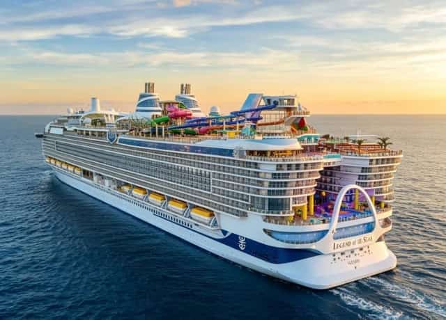 A large Royal Caribbean cruise ship with waterslides sailing at sunset