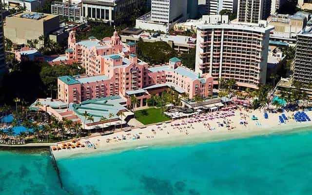 Aerial view of the pink Royal Hawaiian hotel on Waikiki Beach beside turquoise ocean water