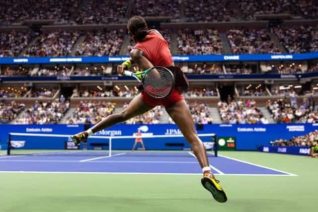 A tennis player leaping for a shot during a packed US Open match in Arthur Ashe Stadium