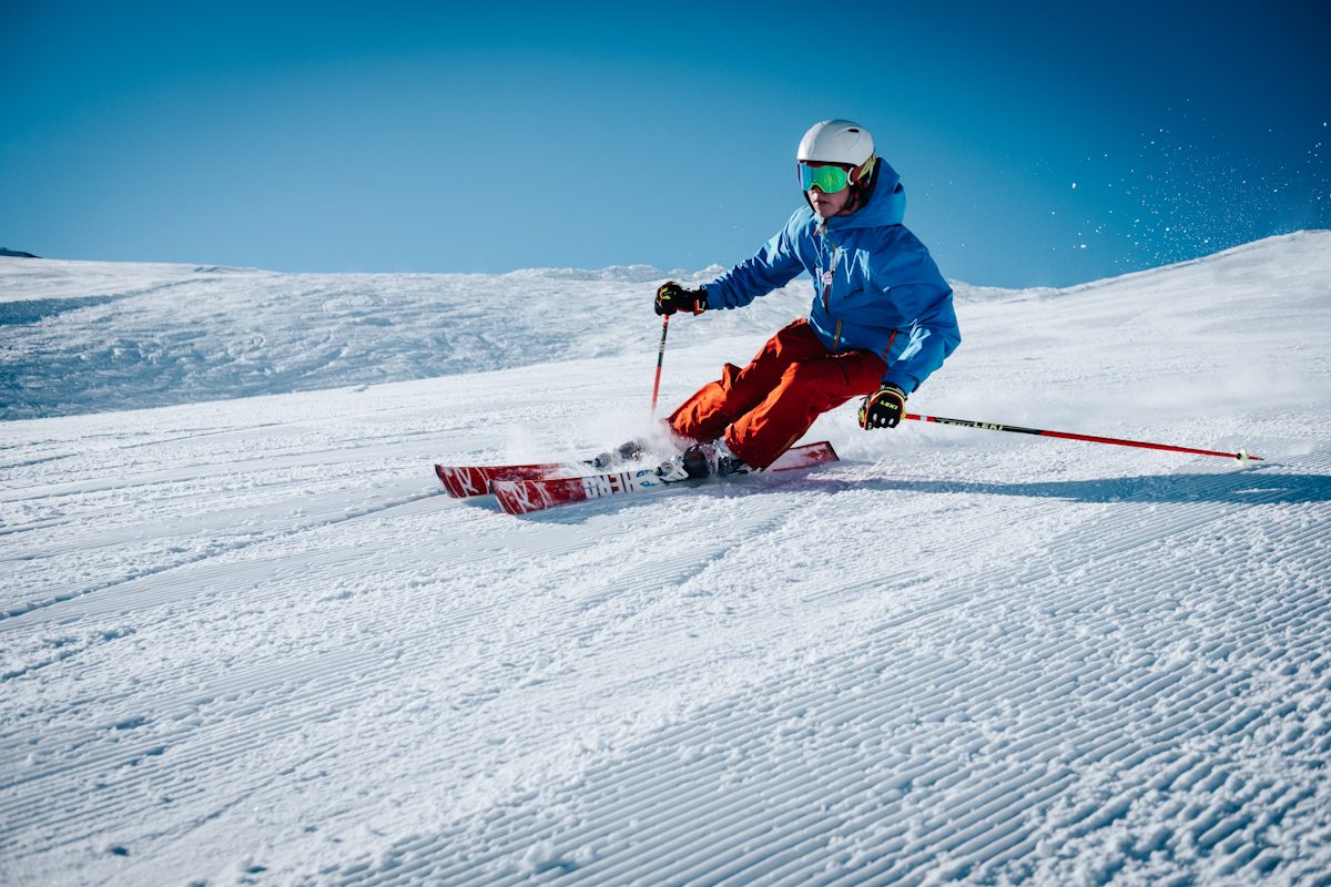 Skiers descending a wide snowy Vail run with the Gore Range and pine forest in the background