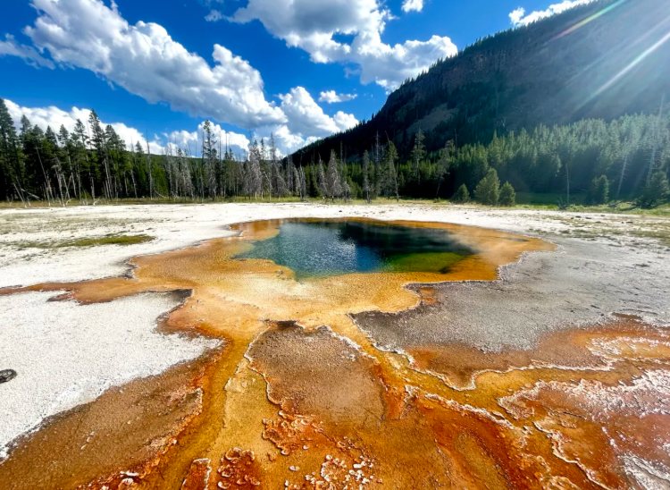 A colorful geothermal hot spring with orange microbial mats under a blue terracotta in Yellowstone
